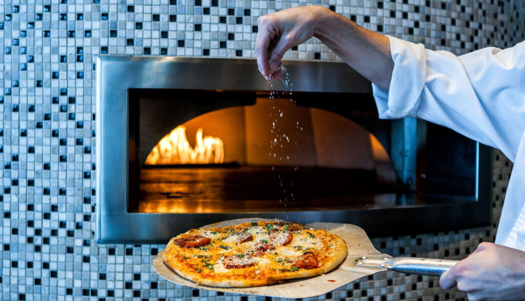 A chef preps a pizza before pushing it into a wood-fired oven.