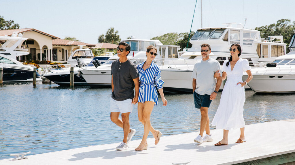 A group of friends walk the marina dock to board a luxury yacht.