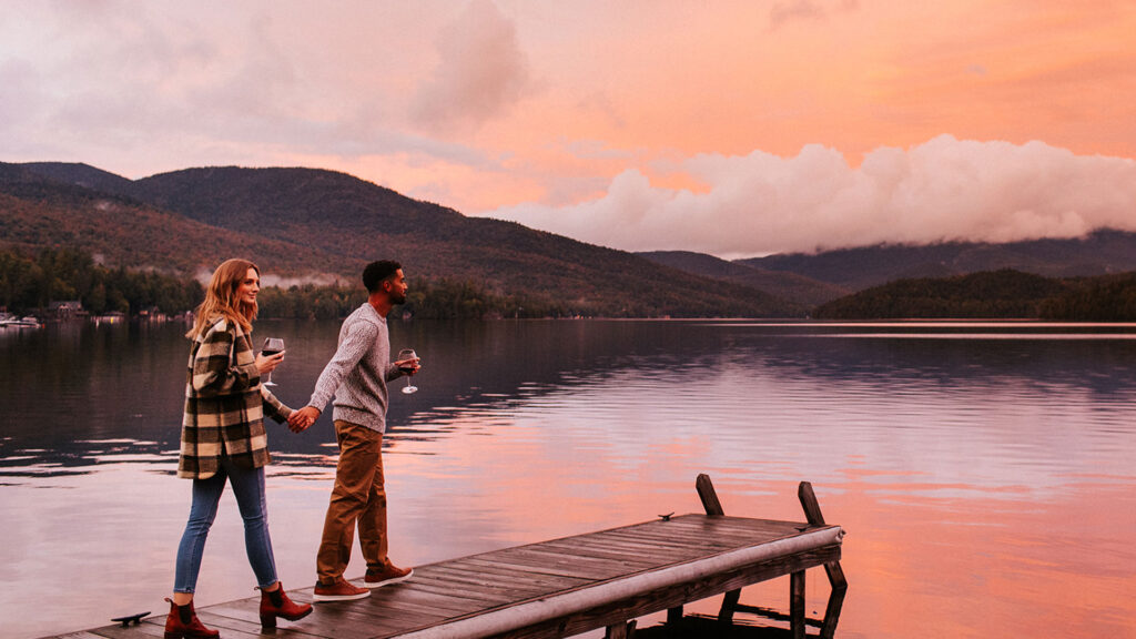 A couple strolls to the edge of the dock at Lake Placid Lodge at sunset.