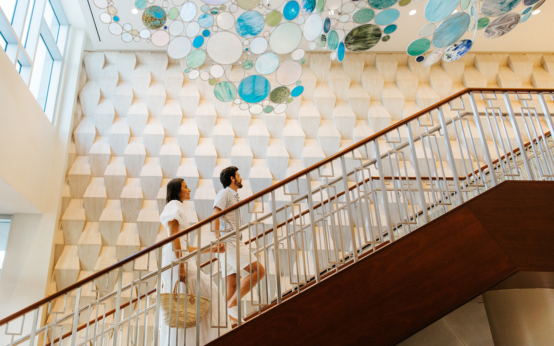 A couple walks up a modern staircase decorated with geometric patterns and colorful circular art pieces at Opal Sands in Clearwater Beach, Florida.