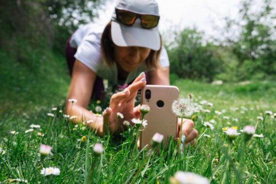 A woman takes a close-up photo of a flower for a photography scavenger hunt challenge.