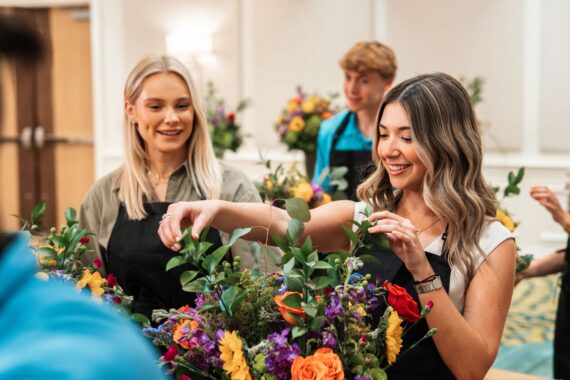 Two women make floral arrangements.