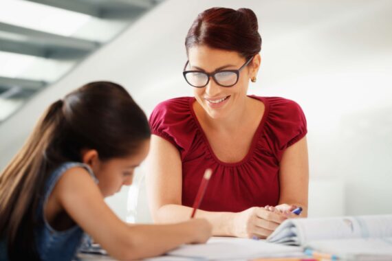 A woman helps a young girl with her homework.
